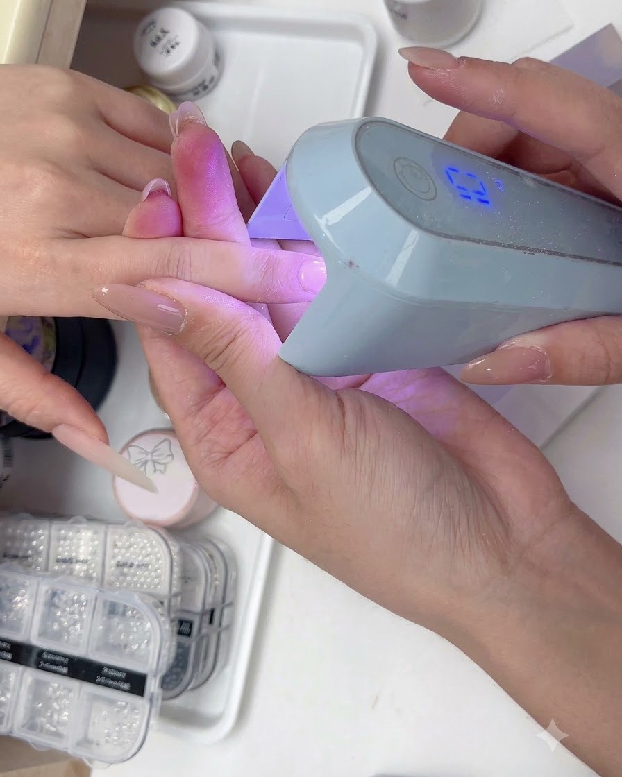 블루 UV/LED 네일 램프 아래에서 컬러 젤 층을 경화하고 있는 손의 모습.