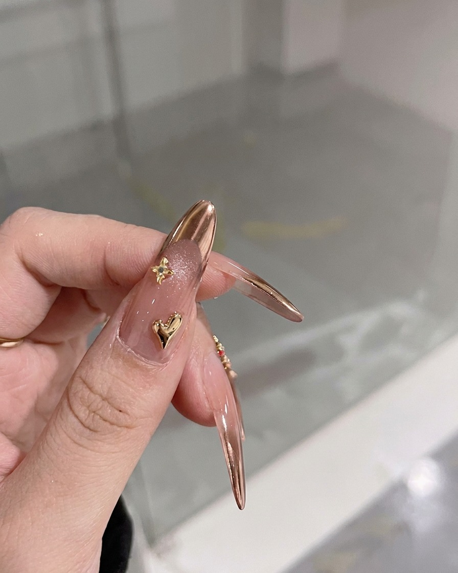 큐티클 부근에 작은 3D 골드 하트 참이 장식된 손가락의 클로즈업 뷰.