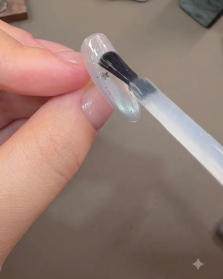 완성된 네일 연장 위로 임베딩된 별 글리터 조각들 위에 브러시로 도톰한 빌더 젤을 도포하는 모습.