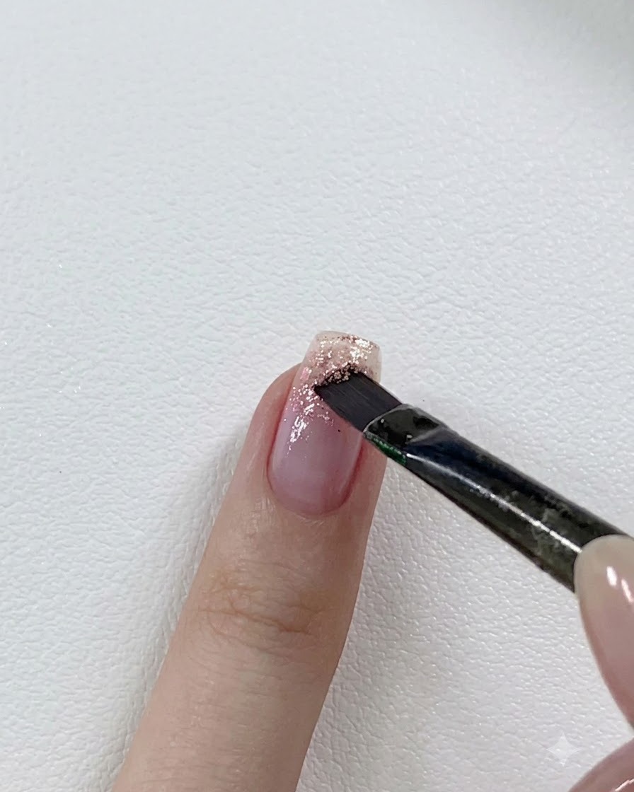 일부 글리터가 발린 손톱 끝에 조금 더 진한 핑크 글리터 젤을 레이어링하는 네일 브러시.