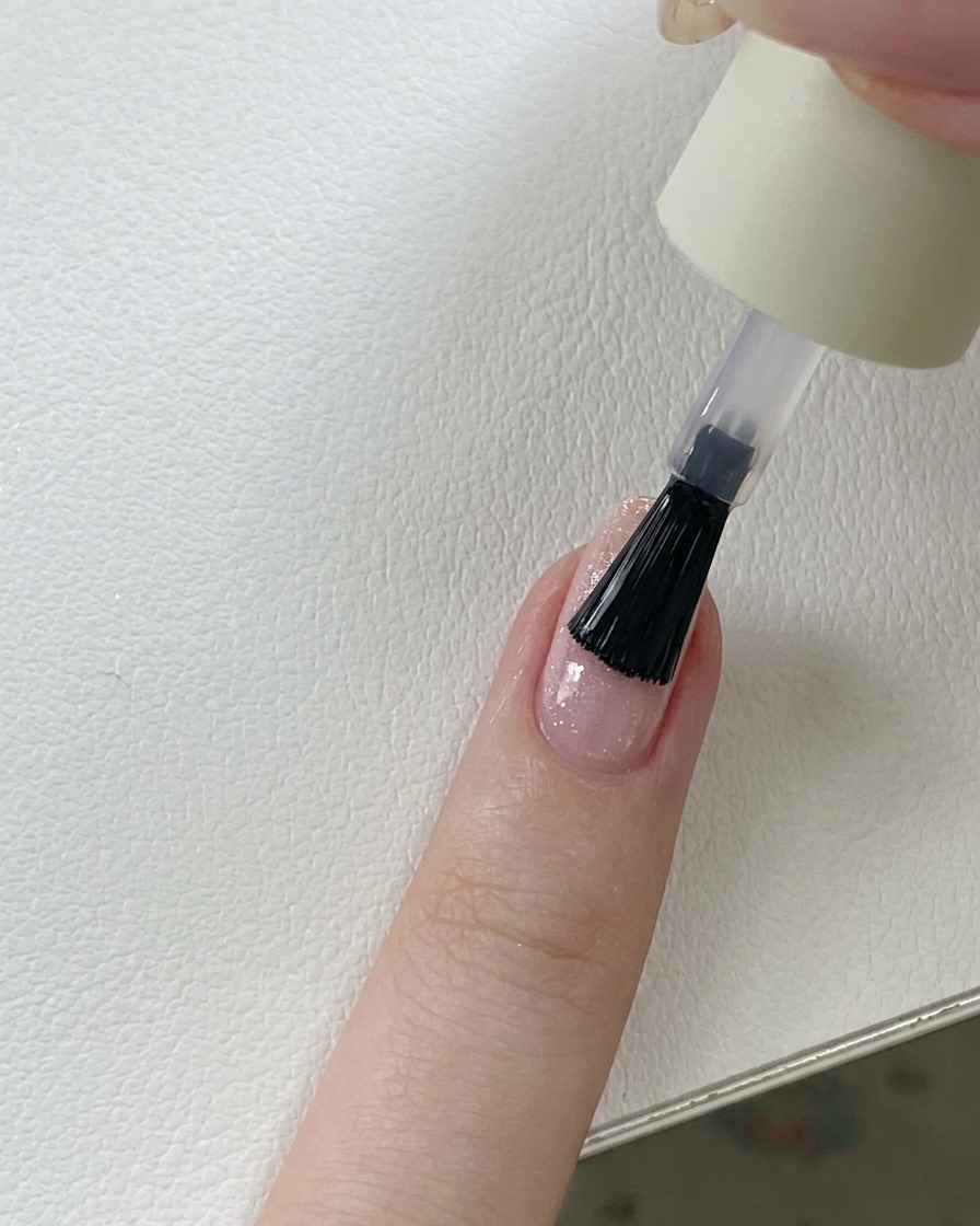 핑크 글리터 젤 네일 위에 투명하고 광택 있는 탑코트를 바르는 브러시.