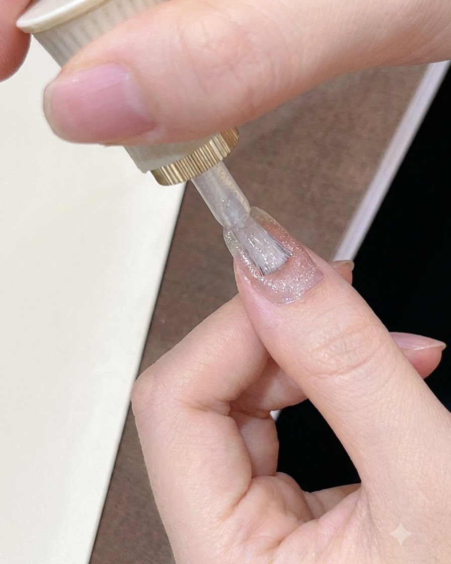 손톱 표면 전체에 은은하게 빛나는 시어한 핑크빛 브라운 젤 폴리시를 브러시로 바르는 모습.