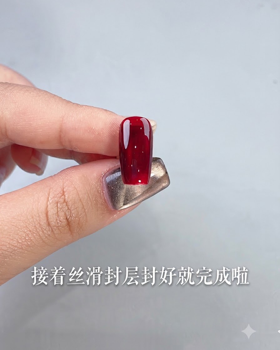 광택이 나는 옥스블러드 레드 젤 폴리쉬로 완성된 단일 네일을 손가락으로 들고 밝은 배경 앞에 있는 모습.