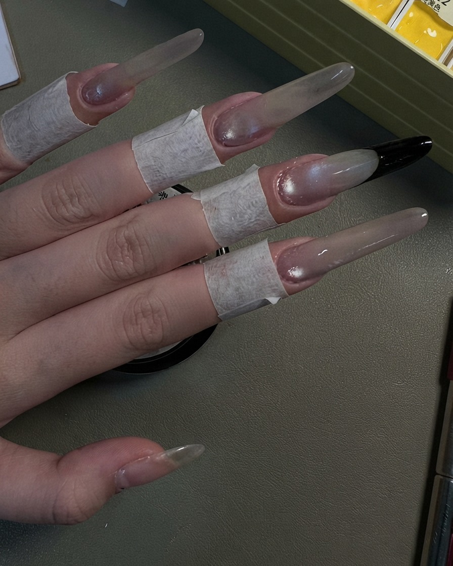 진주빛 그레이 캣츠아이 쉬머 효과가 완성된 네 개의 긴 스틸레토 네일을 보여주는 손.