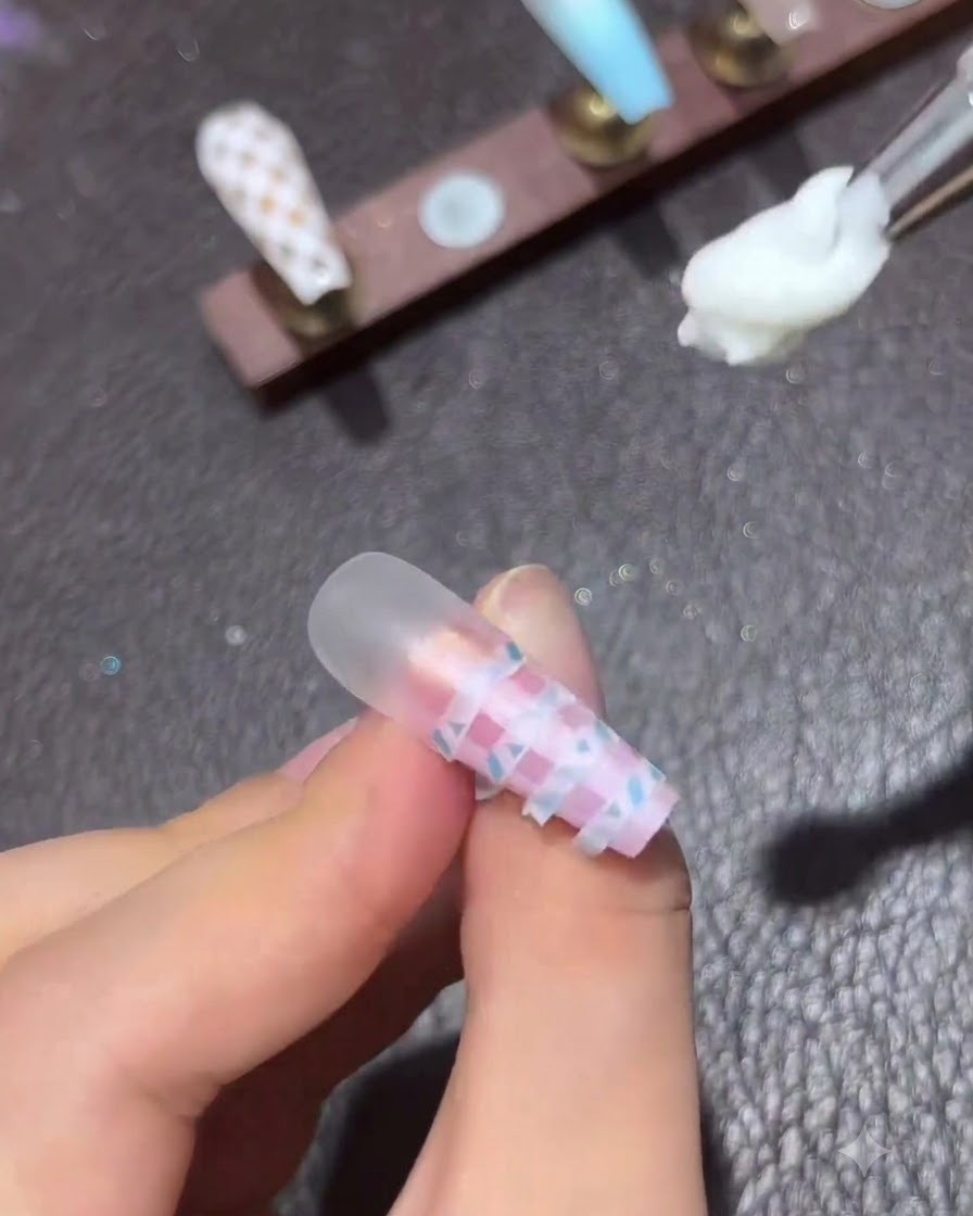완성된 핑크 및 블루 그라데이션 체크 네일 위에서 클리어 젤 탑 코트가 달린 작은 네일 아트 브러시가 떠 있는 모습.
