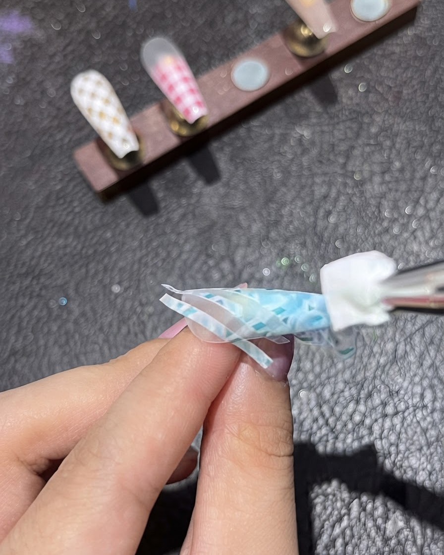 스폰지 툴이 블루 네일 디자인의 두 번째 스트라이프 테이프 층 위에 화이트 피그먼트를 톡톡 두드려 바르는 모습.