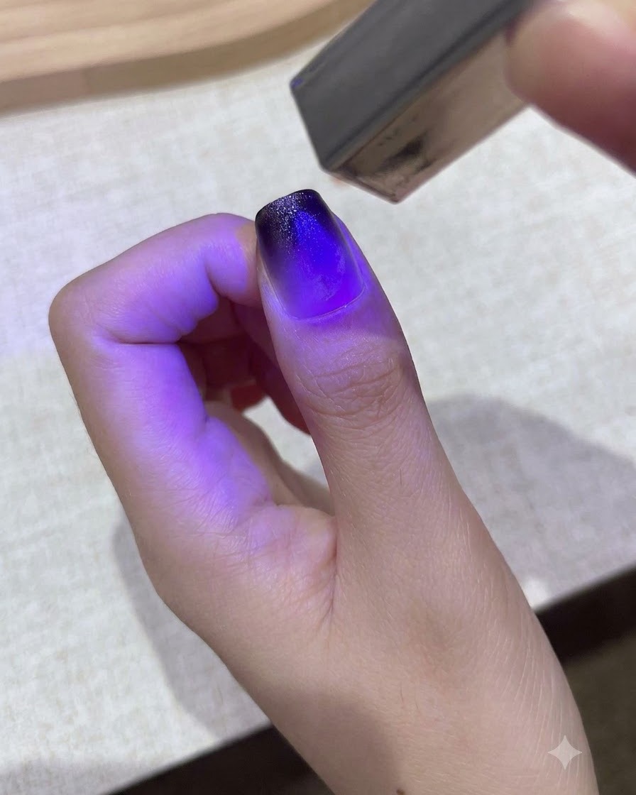 작은 보라색 휴대용 UV/LED 램프가 엄지손톱의 그라데이션 젤 디자인을 경화하는 모습.
