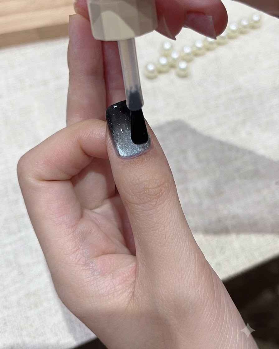 브러시가 완성된 캣아이 네일 디자인 위로 투명한 글로시 탑 코트를 부드럽게 펴 바르는 모습.