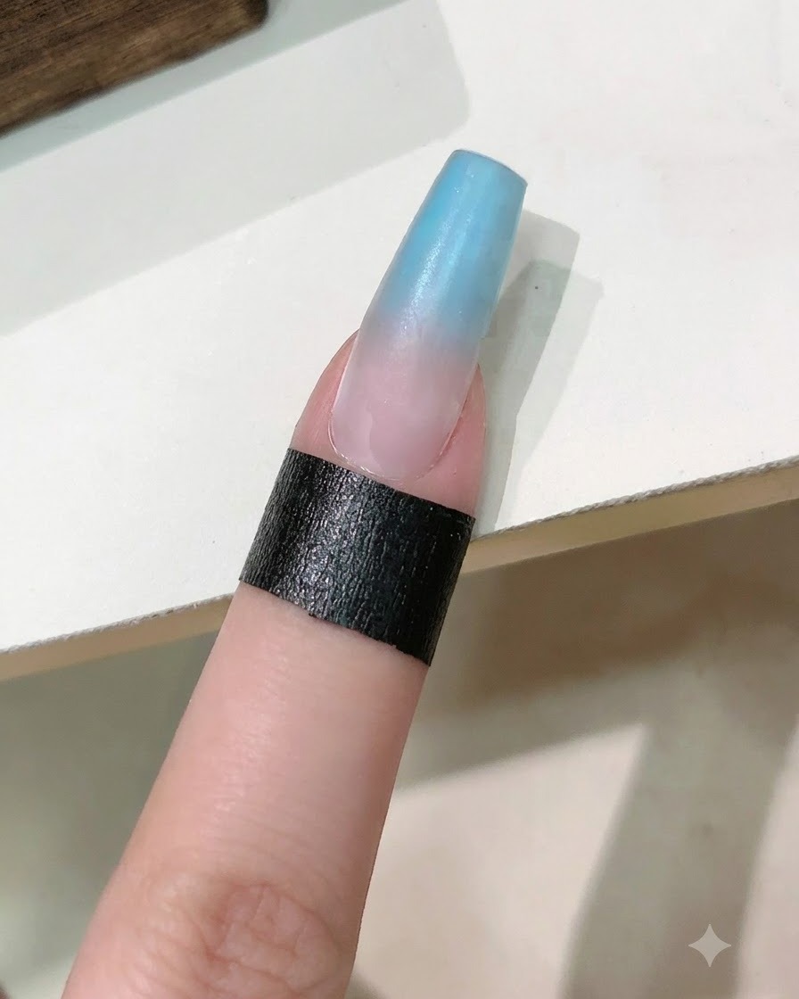네일 브러시가 블루와 핑크 그라데이션 네일 위에 클리어 리인포싱 젤 코트를 바르는 모습.