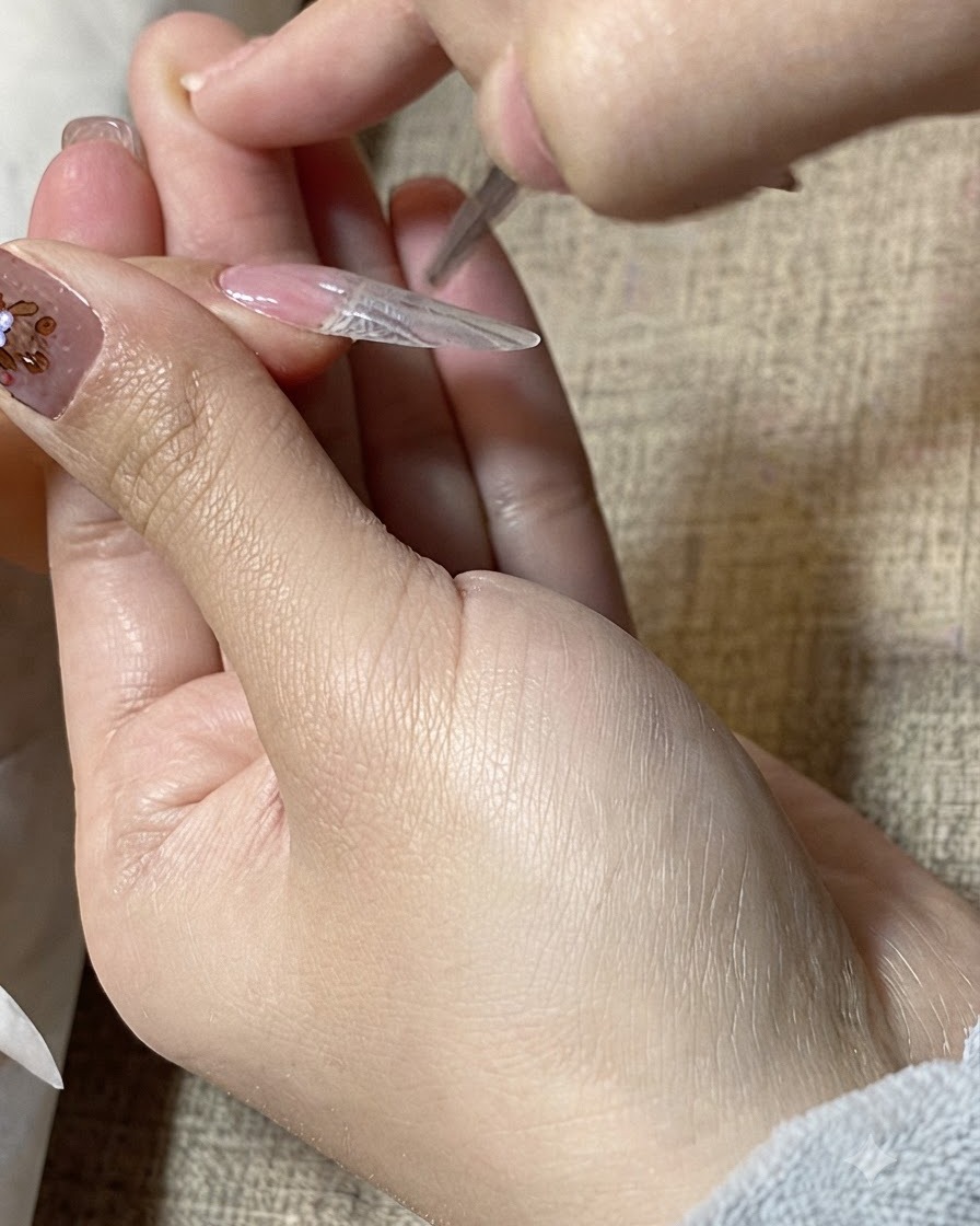 디테일링 브러시가 네일 연장 표면 위로 투명한 젤을 매끄럽게 정돈하는 클로즈업 샷.