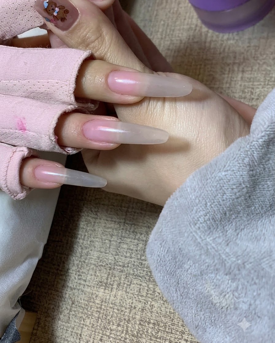 네일 연장 위에 스펀지 패팅 기법으로 부드러운 누드 그라데이션 효과를 표현하는 손 모습.