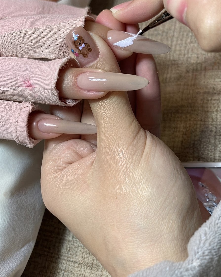 네일 아티스트의 손이 길쭉한 네일 위에서 화이트 나비 날개 패턴을 정교하게 다듬는 모습.