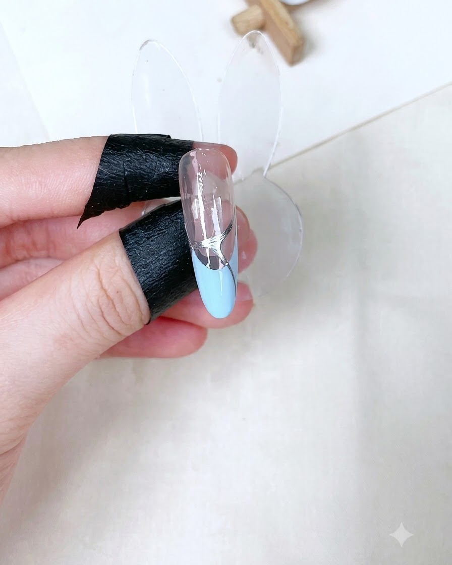 베이비 블루 프렌치 위에 실버 디테일이 들어가 있고 글로시한 클리어 탑젤이 큐어링된 단일 네일 팁 스탠드.