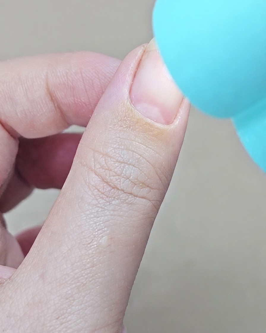 작고 파란색 UV/LED 휴대용 램프가 손톱 바로 위에서 젤 베이스 코트를 경화하는 모습.
