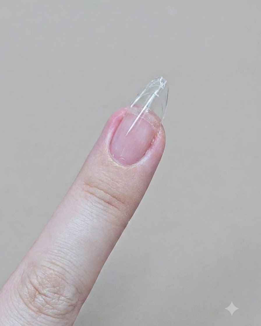 에머리 보드로 클리어 젤 연장이 된 손가락을 날렵한 아몬드 모양으로 파일링하는 모습.