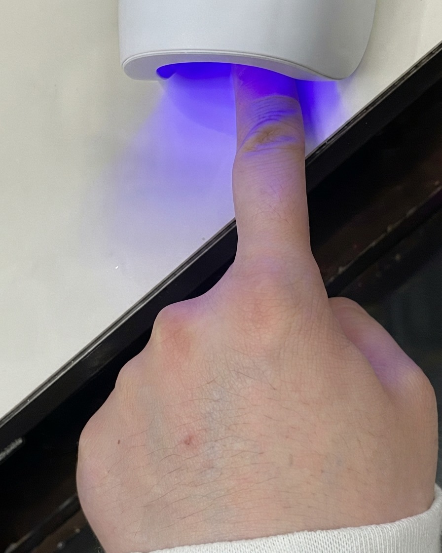 젤 층을 경화하는 미니 UV LED 램프 아래에 손가락을 넣은 모습.