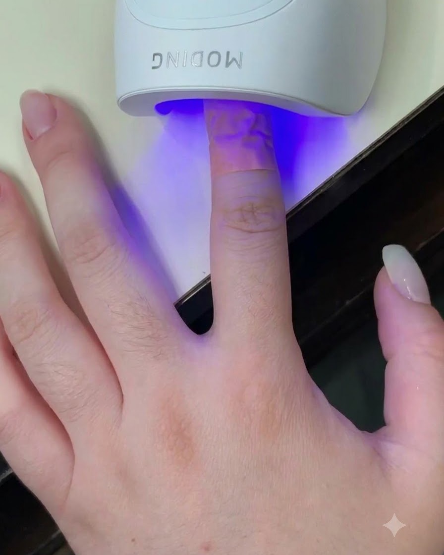 네일에 파란빛이 비치는 하얀색 미니 UV LED 큐어링 램프 안에 손가락을 넣은 모습.