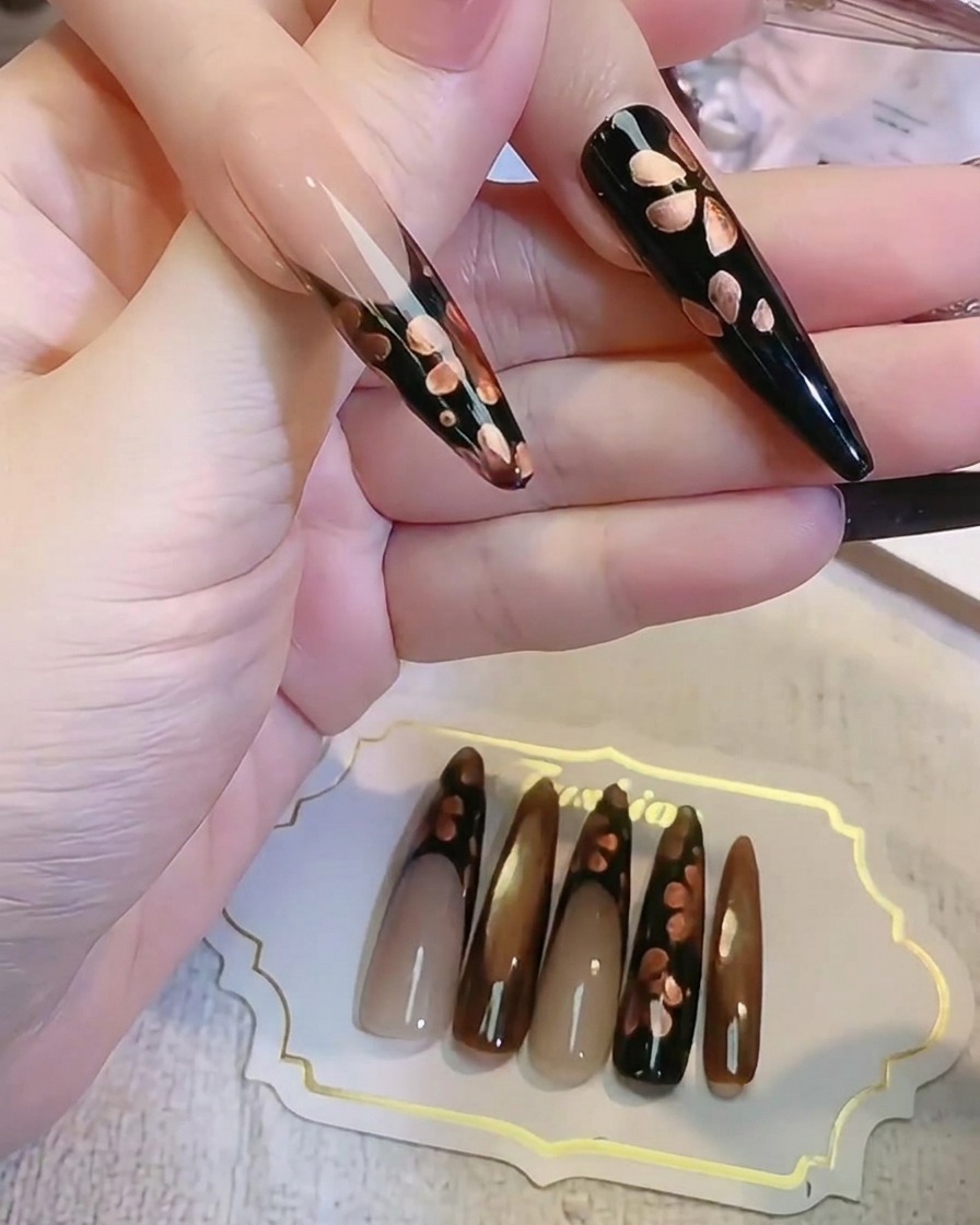 세필 브러시로 다크 블랙 네일 표면에 메탈릭 브론즈 꽃잎 디테일을 그리고 있는 모습.