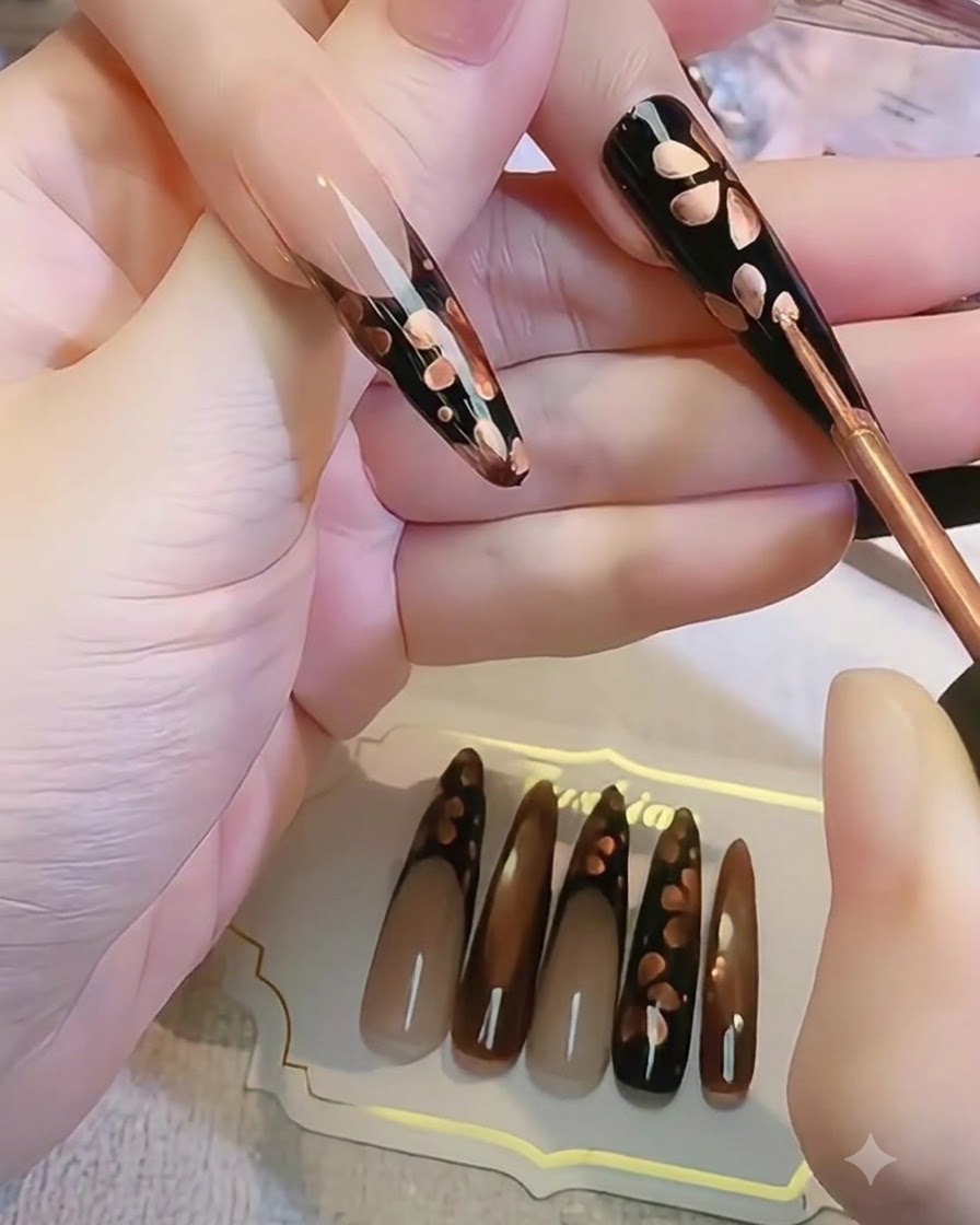 블랙 네일 위에서 세밀한 브러시로 블루밍 메탈릭 꽃잎 모양을 만드는 클로즈업 샷.