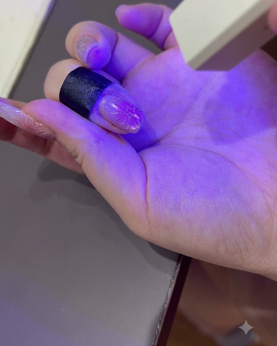 휴대용 UV/LED 네일 램프의 보라색 불빛 아래서 손톱을 큐어링하는 네일 아트된 손.