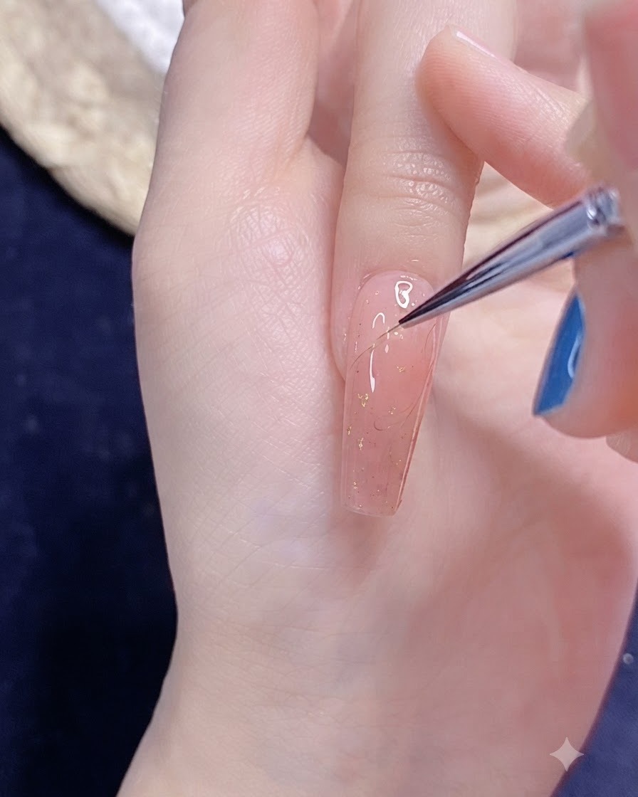 핑크빛이 도는 손톱 위에 세밀한 네일 아트 브러시로 정교한 반쪽 하트 아웃라인을 그리는 모습.