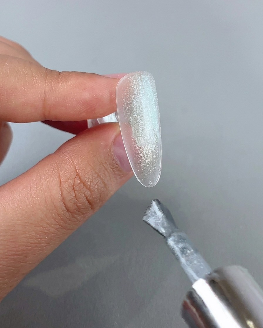 투명한 네일 팁 위에 반짝이는 실버 캣아이 젤을 네일 브러시로 도포하는 모습.