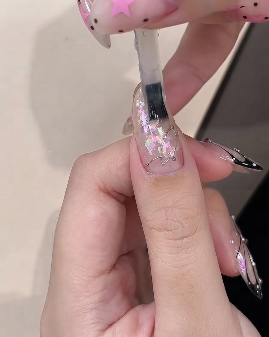 클리어 코팅된 네일에 장식용 오팔 조각 위로 빌더 젤을 바르는 브러시.