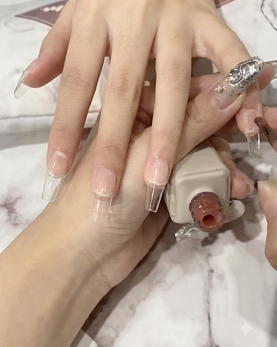 네일 브러시로 긴 코핀 모양의 자연 네일 바디 위에 투명한 누드 젤을 얇게 펴 바르는 모습.