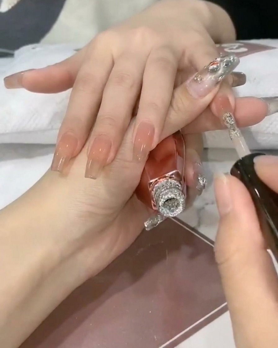 네일 브러시로 투명한 누드 네일 팁 위에 반짝이는 실버 글리터 젤을 얹는 모습.