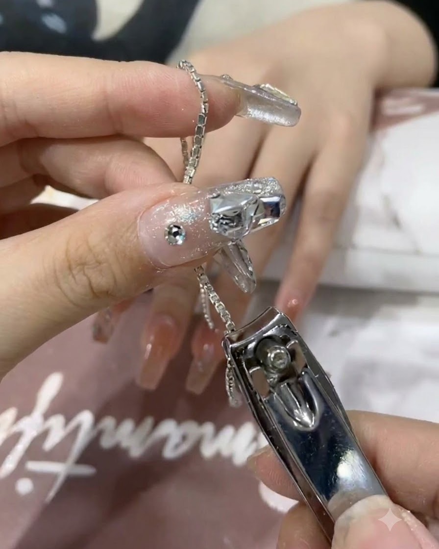 네일 클리퍼로 반짝이는 실버 체인의 짧은 조각을 자르는 클로즈업 샷.