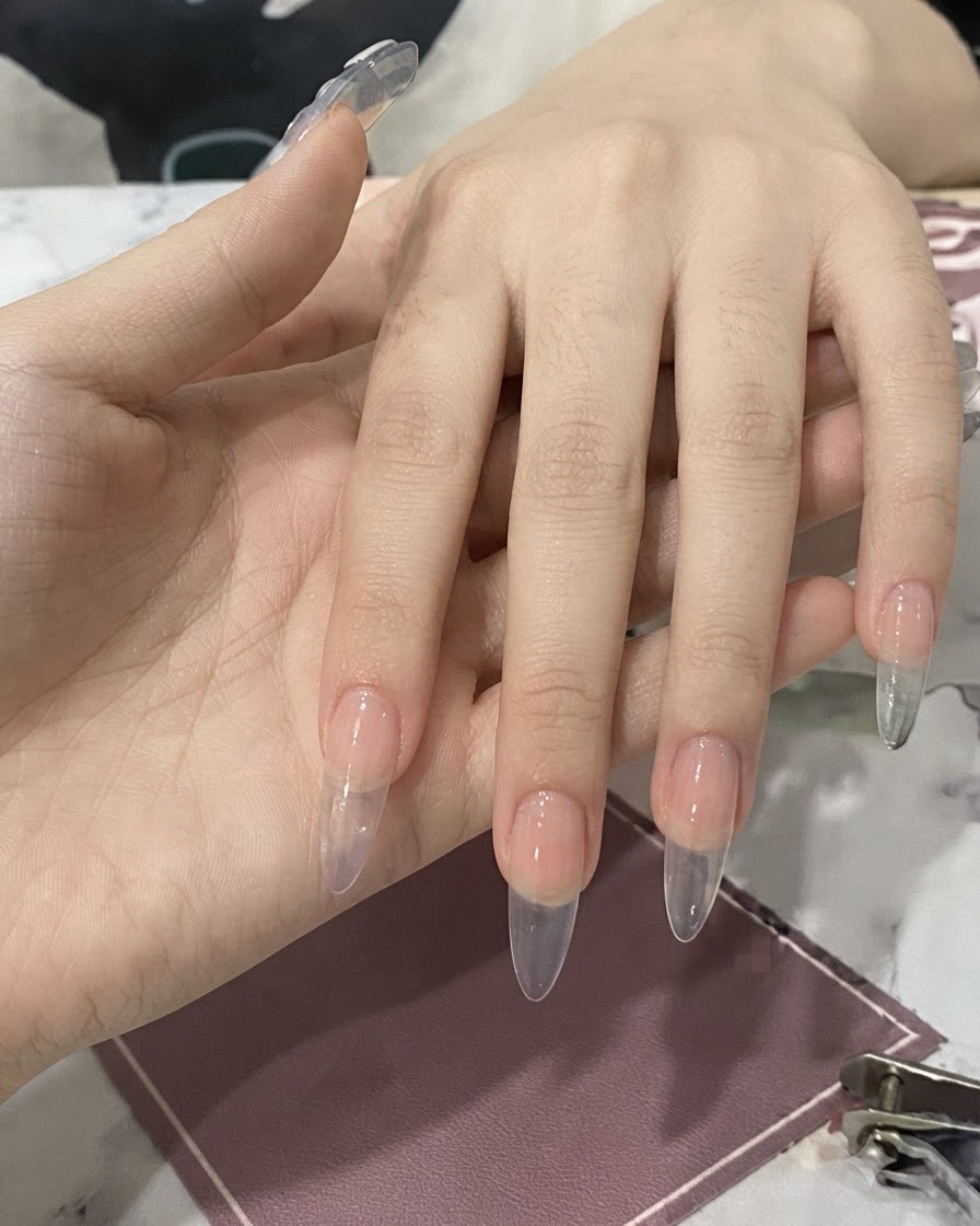 케어된 손톱 위에 브러시가 달린 병을 들고 투명한 네일 글루를 바르는 손의 모습.
