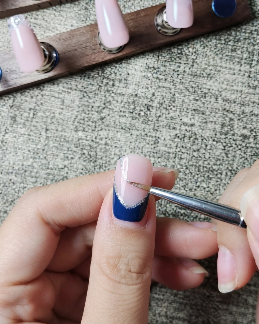 라이너 브러시가 다크 블루 프렌치 팁의 안쪽 가장자리를 따라 얇은 실버 글리터 라인을 세심하게 그리는 모습.