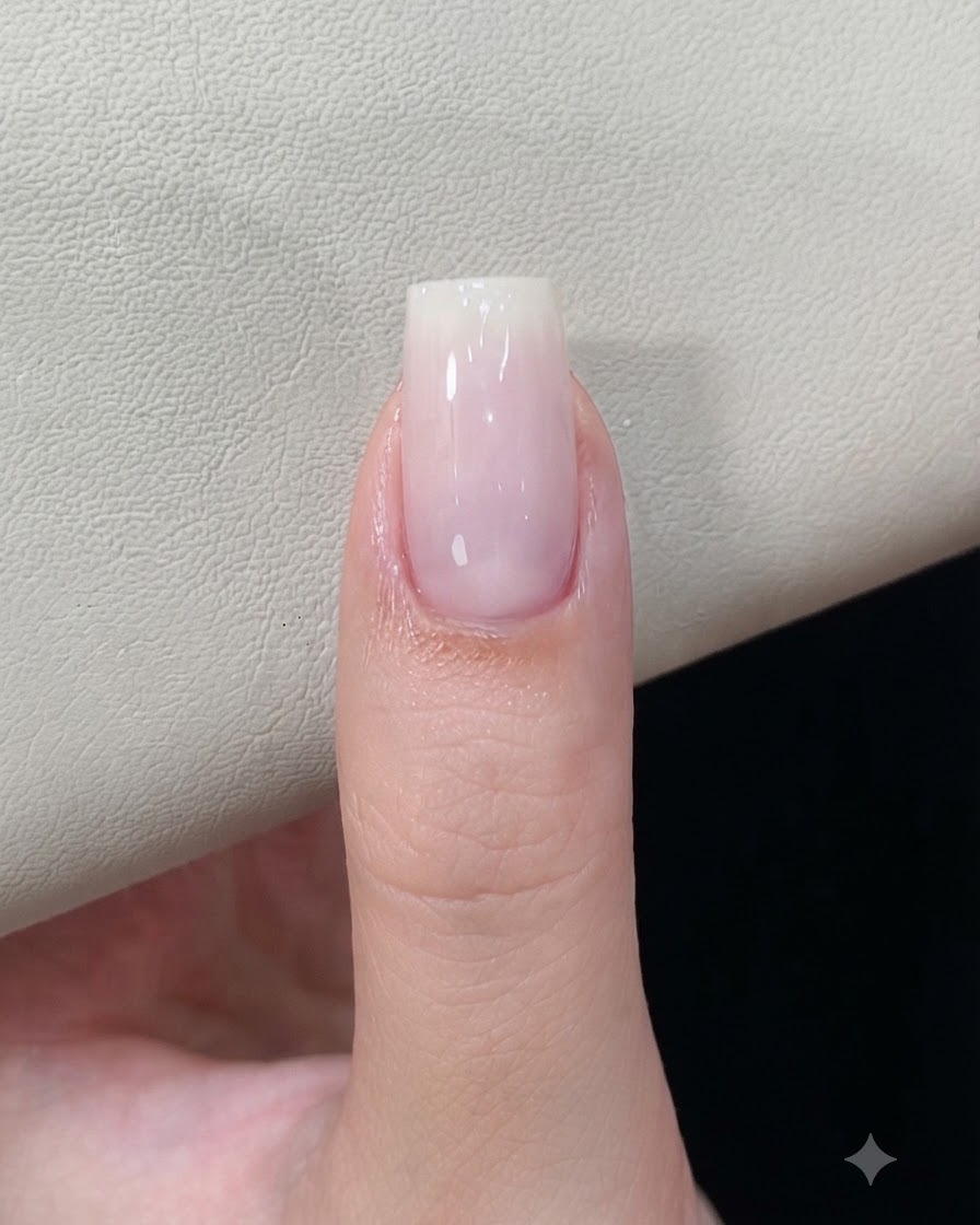 큐어링된 밀키 화이트 젤 베이스를 가진 손톱이 네일 램프 아래에 놓여 있는 모습.