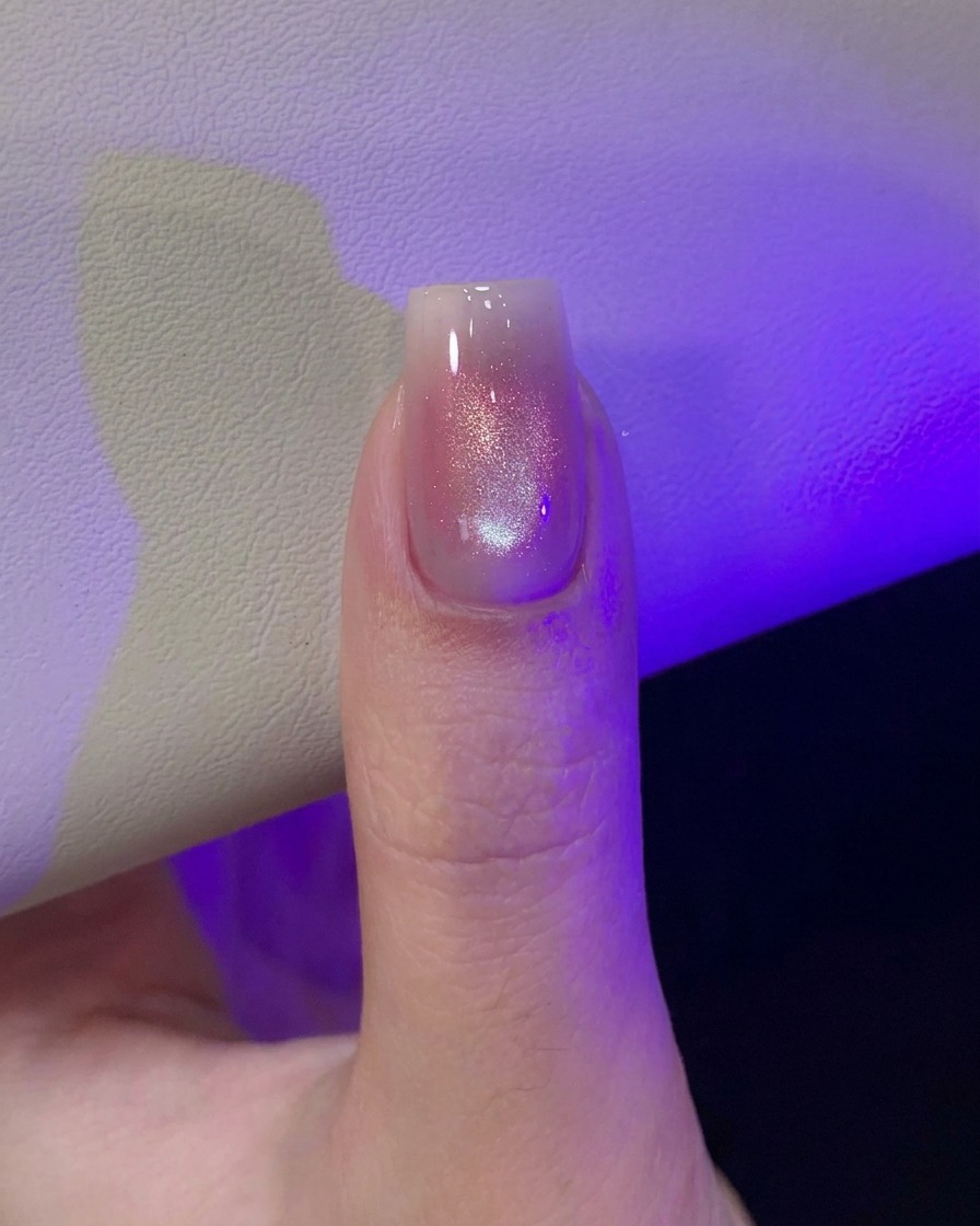 보라색 UV/LED 램프 빛 아래에서 막 자화된 캣아이 네일 디자인을 큐어링하는 엄지손가락.